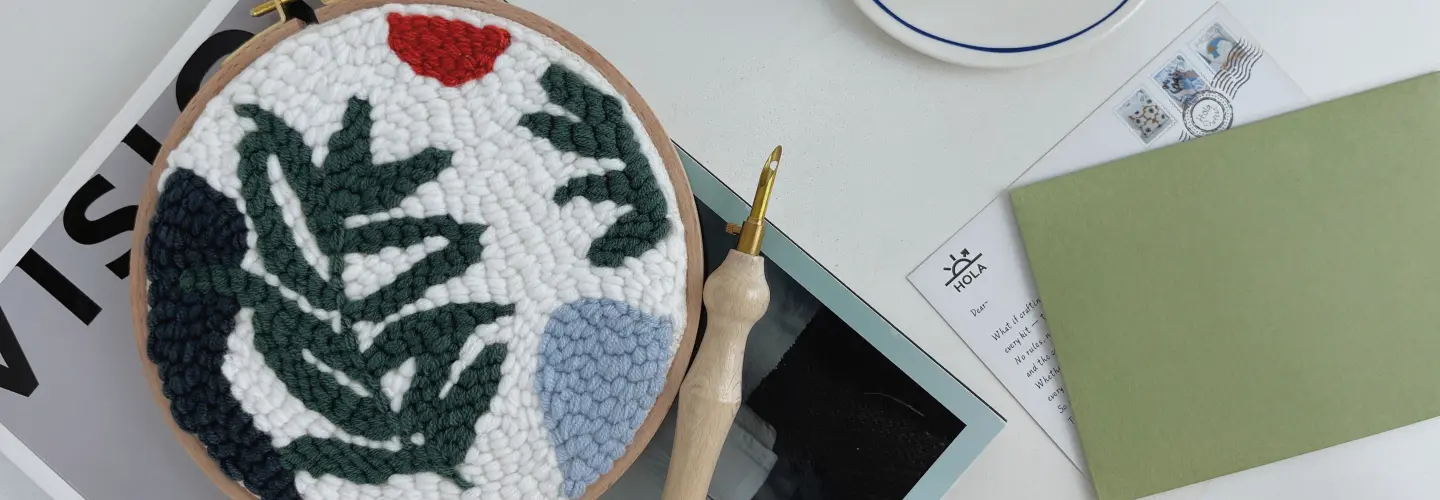 Finished wild leaves punch needle embroidery in wooden hoop with green botanical design and crafting tools on white fabric