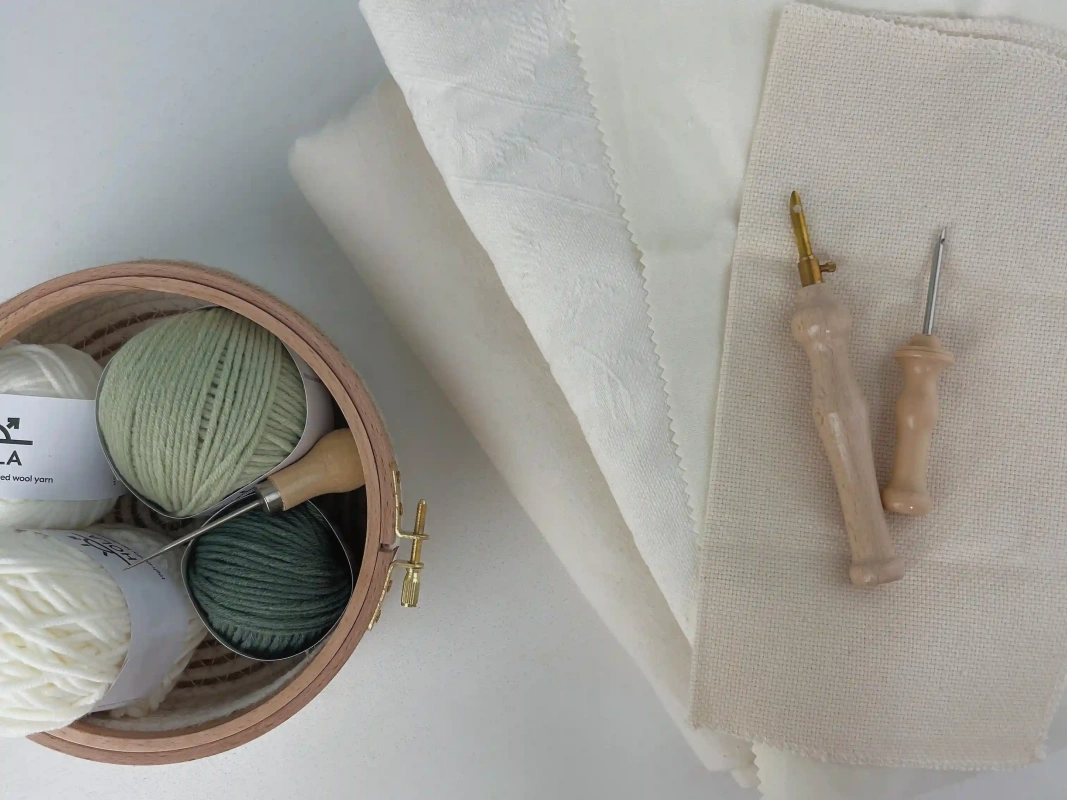 Organized punch needle project supplies with green yarn, wooden hoop, fabric, and wooden punch needle tools