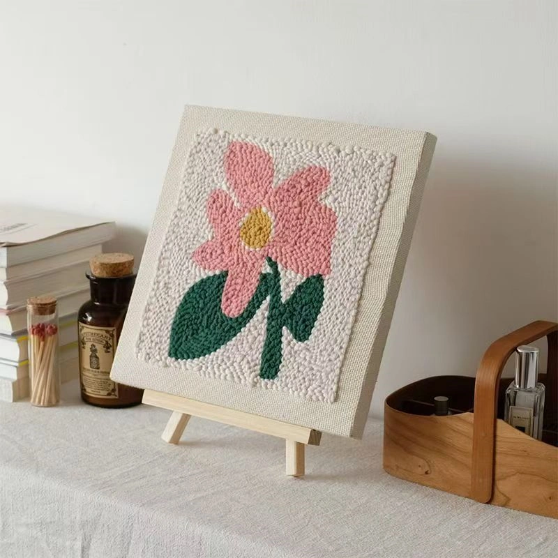Pink Bloom Punch Needle Kit with Stand Display Punch needle flower embroidery on easel with pink bloom and green leaves, displayed in warm room