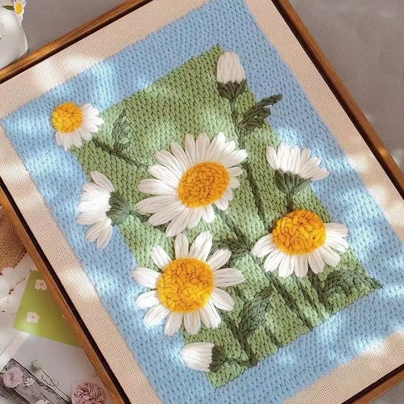 Finished daisy punch needle wall art with white petals and yellow centers, framed with blue and green background.