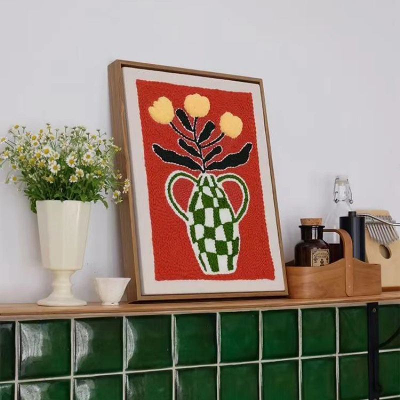 Punch Needle Wall Art Featuring Green Checkered Vase and Yellow Flowers Framed punch needle wall art with a green vase and yellow flowers in bold colors on a red background.