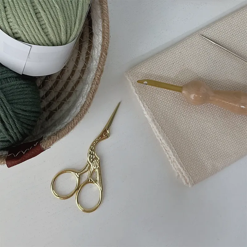 Gold stork embroidery scissors with ornate design on white surface beside yarn and fabric, premium crafting tools