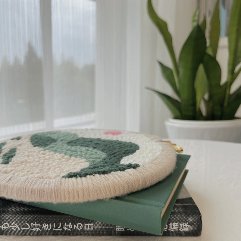 Finished hoop artwork with edge binding laid flat on two books, highlighting tight stitches and clean edging, with a green plant softly visible in the background.