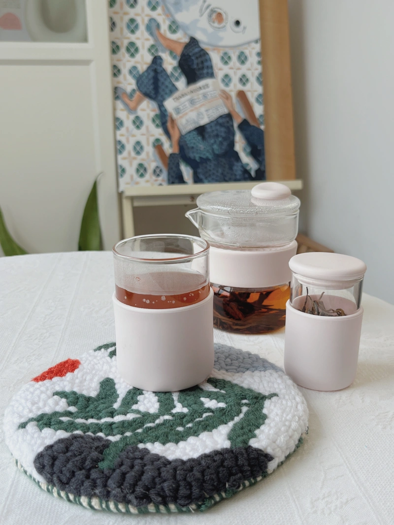 Finished hoop trivet with the Holakits Wild Leaves design, holding a cup of hot tea, with loose tea leaves and a small teapot nearby.
