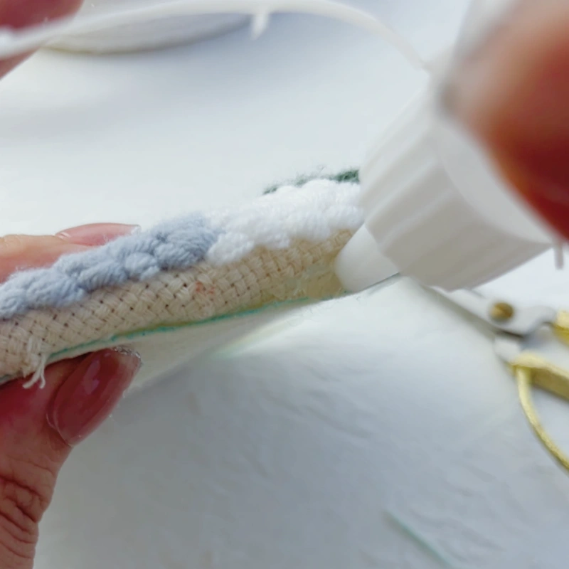 Applying extra glue to areas with insufficient coverage, a detail that is easy to overlook in the punch needle hoop trivet tutorial.