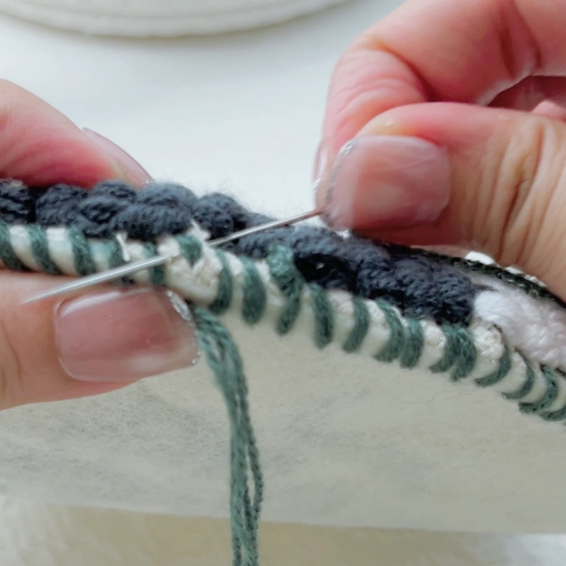 Completing the final stitch by passing the needle through the starting point.