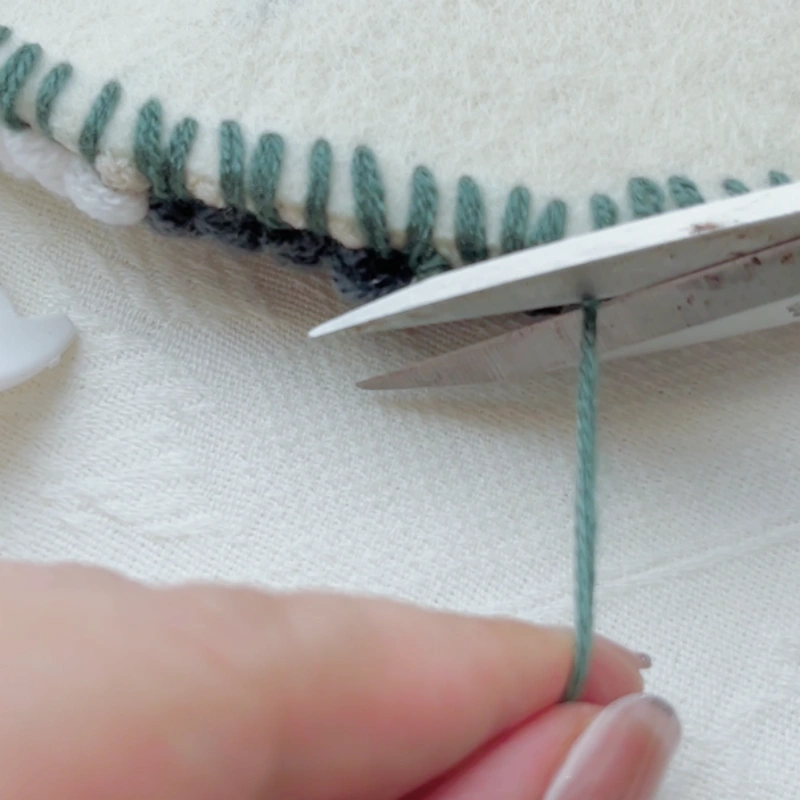 Tying a knot to secure the stitching and trimming excess yarn.