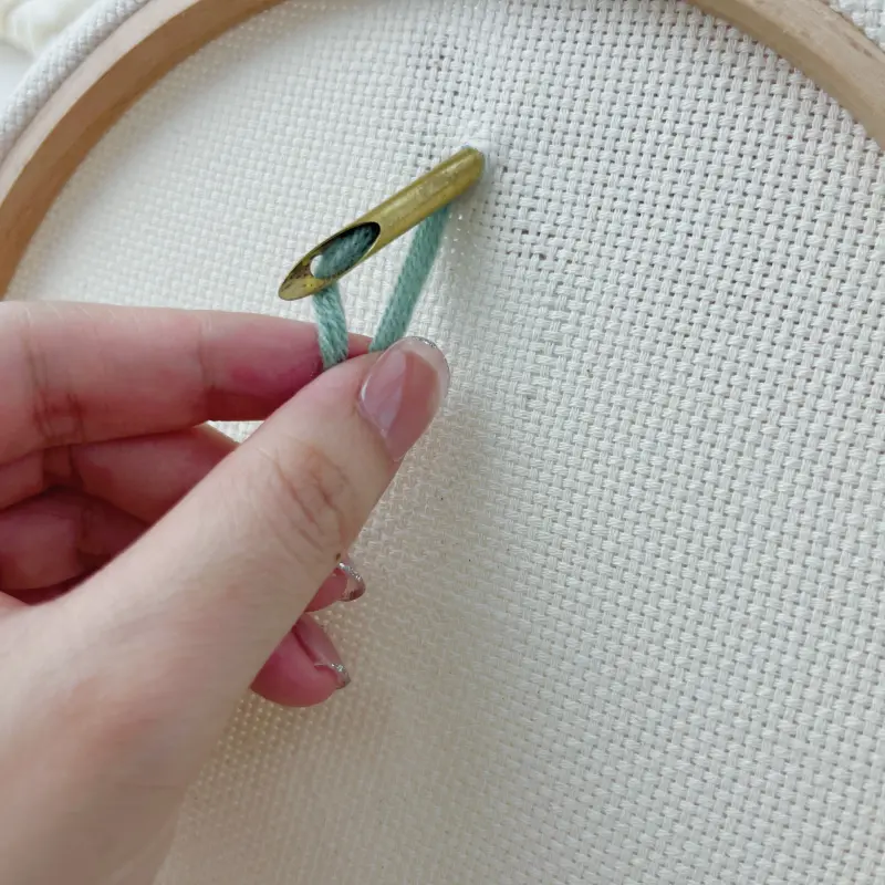 Pulling the yarn tail from the back of the fabric to secure the stitch.