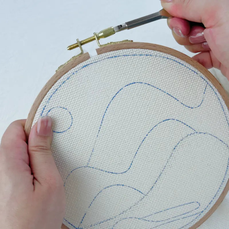 Tightening the hoop screw with a flat head screwdriver to secure the fabric.