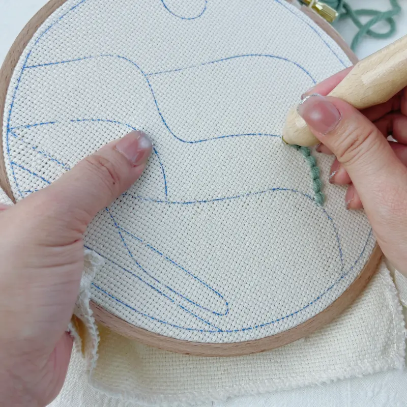 Punching continuously along the pattern outline, fully inserting the punch needle into the fabric with each stitch.