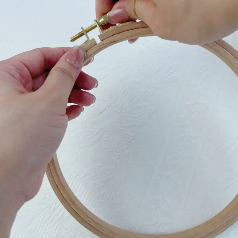 Loosening the metal screw to release tension on the embroidery hoop.